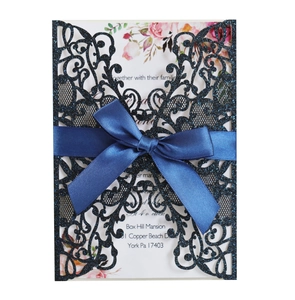 Detail of laser-cut navy glitter wedding invitation with blue satin bow and floral insert
