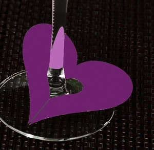 Detail view of a purple heart-shaped paper place card placed on a wine glass stem