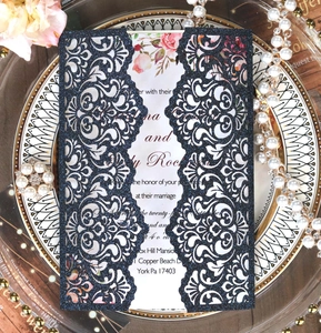 Detail of navy glitter laser-cut wedding invitation with floral insert on gold tray