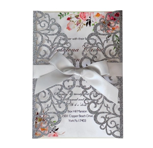 Detail view of laser-cut silver glitter wedding invitation with white satin bow and floral card