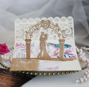 Detail of 3D laser-cut wedding invitation with gold glitter floral arch and couple