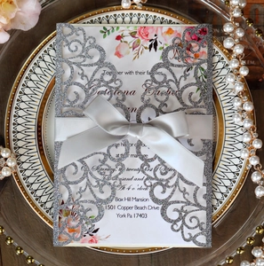 Close-up of laser-cut silver glitter wedding invitation with floral card and satin bow