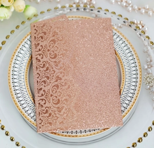 Detailed laser-cut rose gold glitter invitation card placed on elegant decorative plates