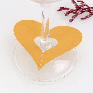 Detail of laser-cut heart place card in sparkling gold paper for wedding wine glasses