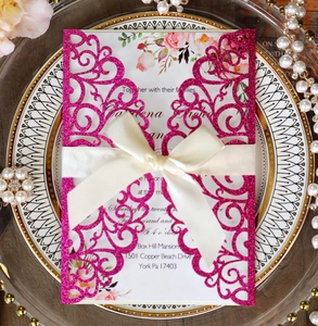 Detail of laser-cut wedding invitation with pink glitter paper and white satin ribbon bow