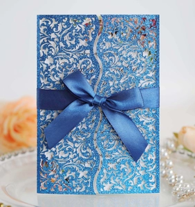 Detail of blue glitter laser cut wedding invitation with navy ribbon and floral pattern