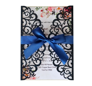Macro shot of navy glitter laser-cut wedding invitation with satin ribbon and floral insert