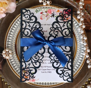 Detail of navy laser-cut wedding invitation with floral insert and satin ribbon bow