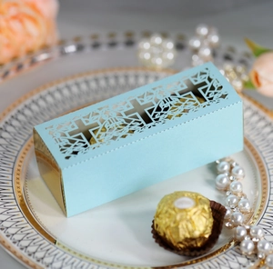 Detail of light blue laser-cut favor box with cross pattern and golden chocolates