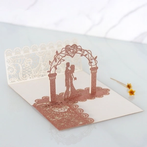 Detail of laser-cut 3D pop-up wedding card featuring rose gold glitter and a romantic archway