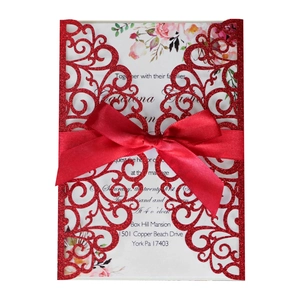 Detail of laser-cut red glitter wedding invitation with satin bow and floral insert