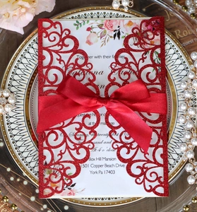 Close-up of red glitter laser-cut wedding invitation with elegant satin ribbon bow