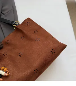 Detail of brown suede tote with hollow floral patterns and wooden bead accessory