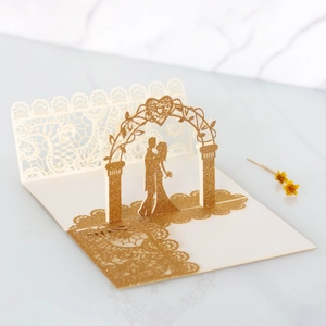 Macro detail of laser-cut 3D wedding invitation with gold glitter and bridal couple