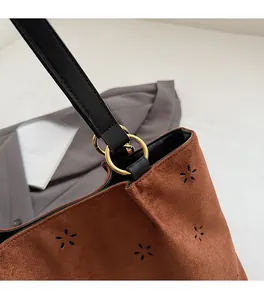 Detail of laser-cut floral pattern on brown suede tote with gold hardware and leather strap