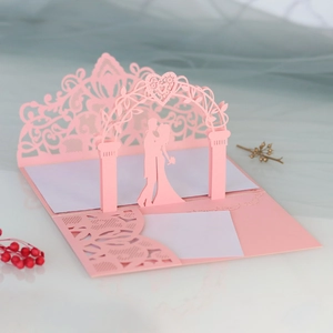 Close-up of 3D pop-up wedding invitation card with laser-cut kissing couple under an arch