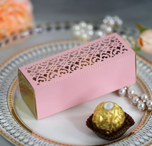 Pink laser-cut candy box with ornate patterns shown next to chocolate and pearls