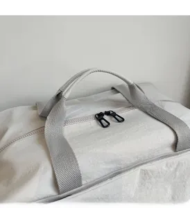 Detailed close-up of cream nylon fabric texture and sturdy grey strap of the travel bag