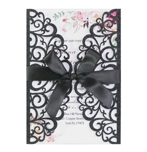 Macro detail of laser-cut glitter wedding invitation with black satin ribbon bow