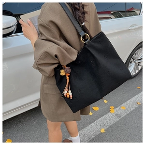 Détail d'un sac cabas en daim noir avec motifs étoiles ajourés et pompons colorés