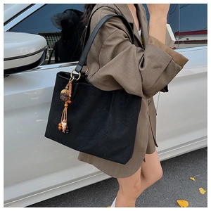 Détail du sac cabas en daim noir avec motifs ajourés et pendentif pompon de style bohème