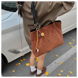 Detail of dark brown suede tote bag with laser-cut floral patterns and tassel charm