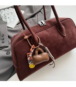 Detail einer burgunderroten Wildledertasche mit Doppelreißverschluss und Taschenanhänger