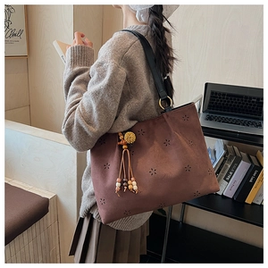 Détail d'un sac cabas en daim marron avec motifs à fleurs ajourés et pompon en perles de bois