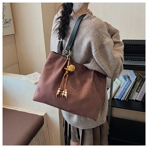 Gros plan du sac cabas en daim marron avec motifs floraux ajourés et pompon décoratif