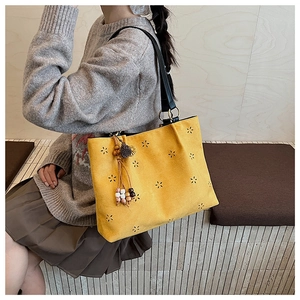 Detail of yellow suede tote bag featuring laser-cut floral patterns and ethnic tassels
