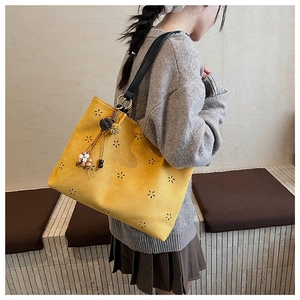 Gros plan sur un sac cabas en daim jaune avec motifs floraux perforés et pompon ethnique