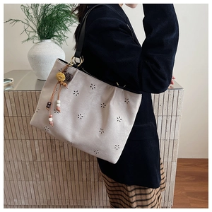 Detail of laser-cut flower patterns on a beige suede tote bag with ethnic beaded tassel