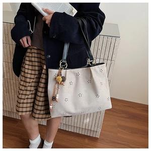 Détail de motif floral évidé et pompon sur cabas en daim beige avec sangle en cuir noir