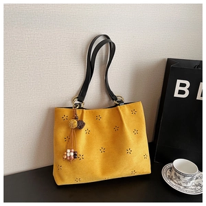 Détail du sac fourre-tout jaune en daim avec motifs floraux découpés au laser et pompon ethnique