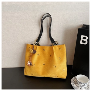 Détail d'un cabas en daim jaune avec découpes florales et breloque à pompons ethnique