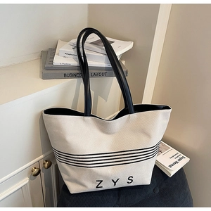 Detail view of cream canvas tote bag with black stripes and ZYS logo on a stylish stool