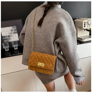 Detail of caramel suede crossbody bag with gold chain and diamond quilting on a model