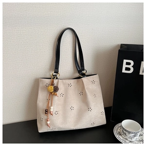 Détail du sac cabas en daim beige avec motifs floraux ajourés et pompon perlé