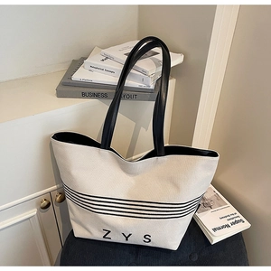 Close-up of large canvas tote with black stripes and leather straps on book stack
