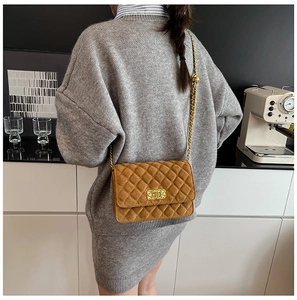 Brown quilted suede crossbody bag with gold chain strap worn by a model in a cafe