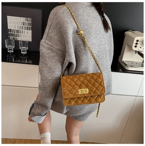 Brown quilted suede crossbody bag with gold chain strap shown on a model in a modern room