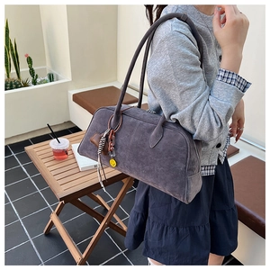 Nahaufnahme einer grauen Vintage-Wildlederhandtasche mit Smiley-Anhänger im Freien