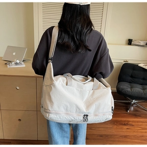 Detail of off-white travel tote showing wide adjustable strap and bottom zipper pocket