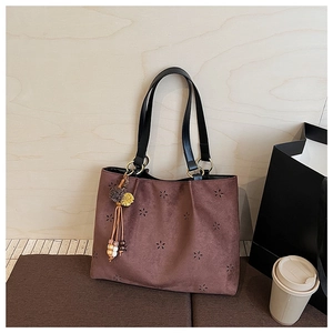 Détail du sac cabas en daim marron avec motifs floraux ajourés et breloque à gland