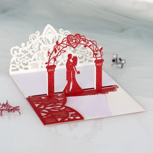Carte de mariage 3D avec arche de cœur rouge pailleté et silhouette de couple découpée au laser