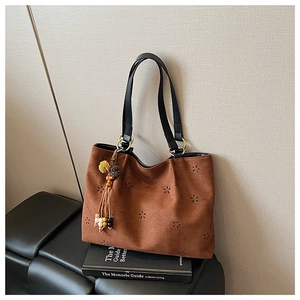 Détail d'un cabas en daim marron avec motifs floraux découpés au laser et pompon