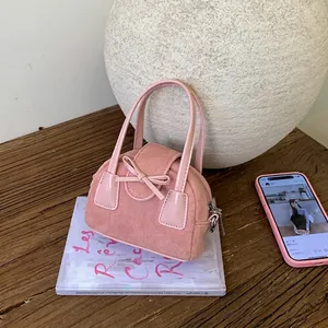 Pink suede crossbody mini bag with bow detail on dark wood table in aesthetic setting