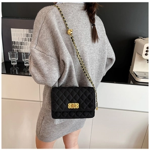 Close-up of a black quilted crossbody bag with a gold chain strap worn by a model