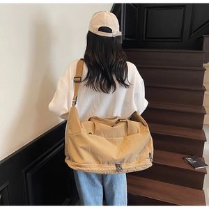 Rear view of model wearing a large khaki travel bag with shoulder strap on stairs