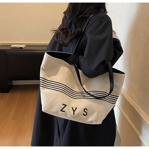 Detailed view of large striped canvas tote bag with black leather straps on a model
